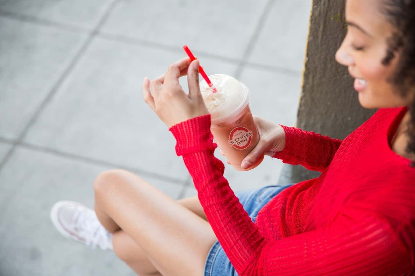 African-American girl in a red sweater enjoying a smoothie from Scooter's Coffee.