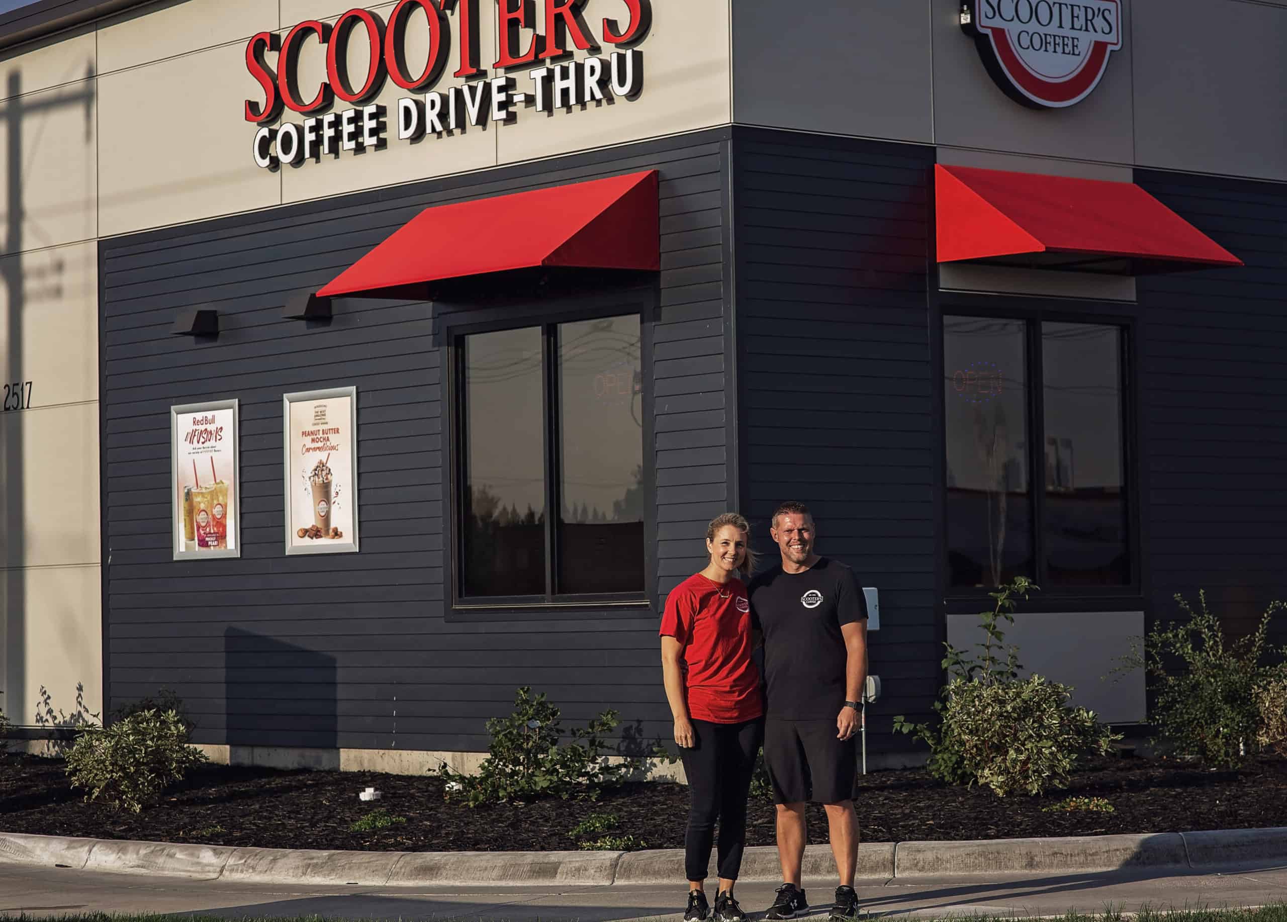 Two Scooter's Coffee franchisees standing in front of their drive-thru coffee franchise.