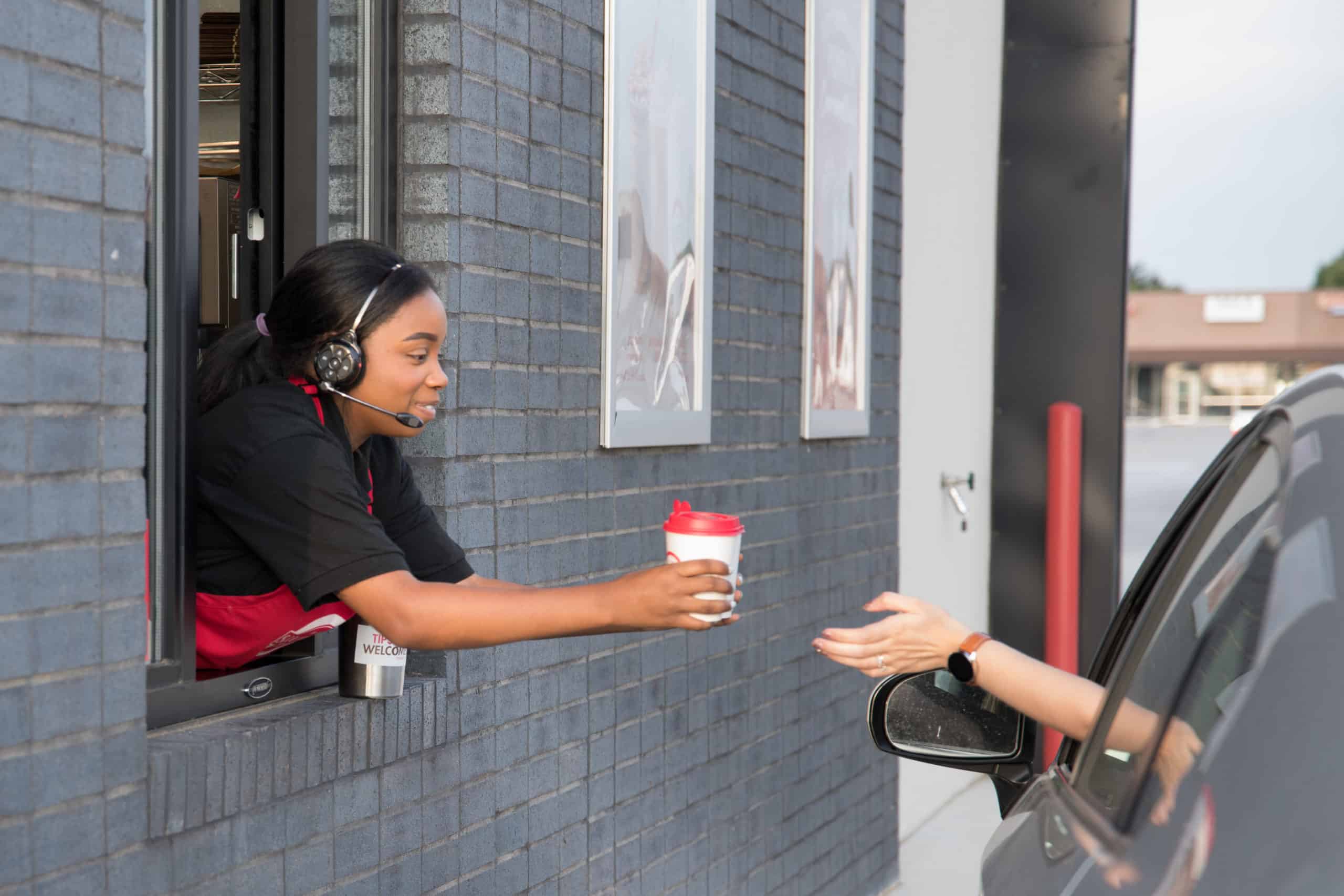 A friendly employee handing a cup of coffee to a customer at a drive-thru coffee shop.