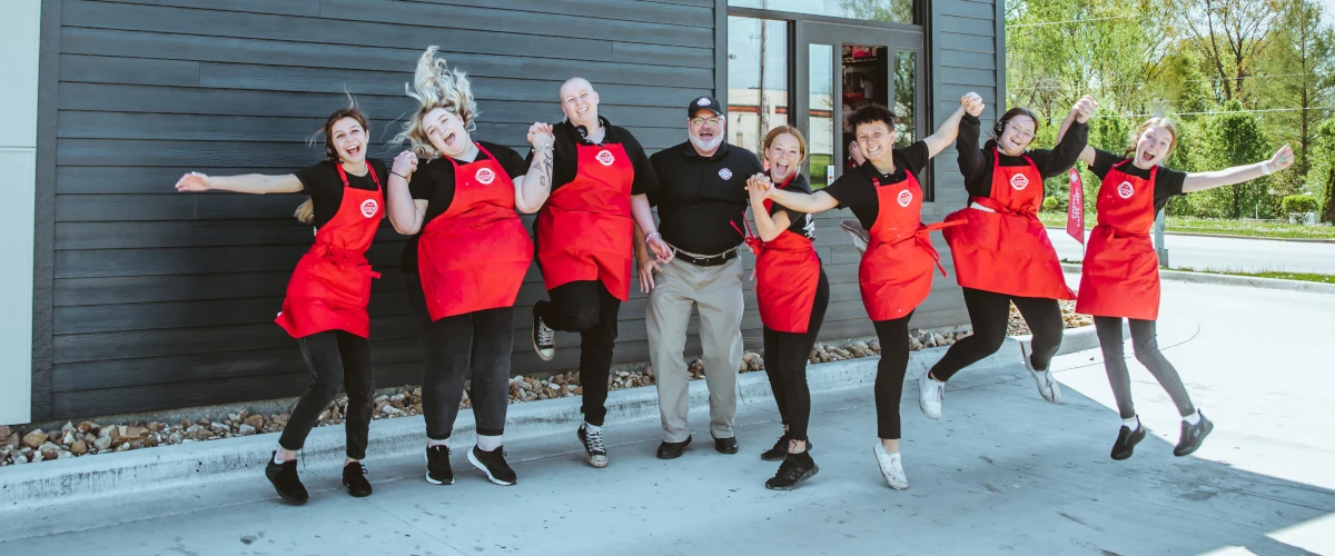 Scooter's Franchise employees holding hands and jumping outside a drive-thru coffee window.