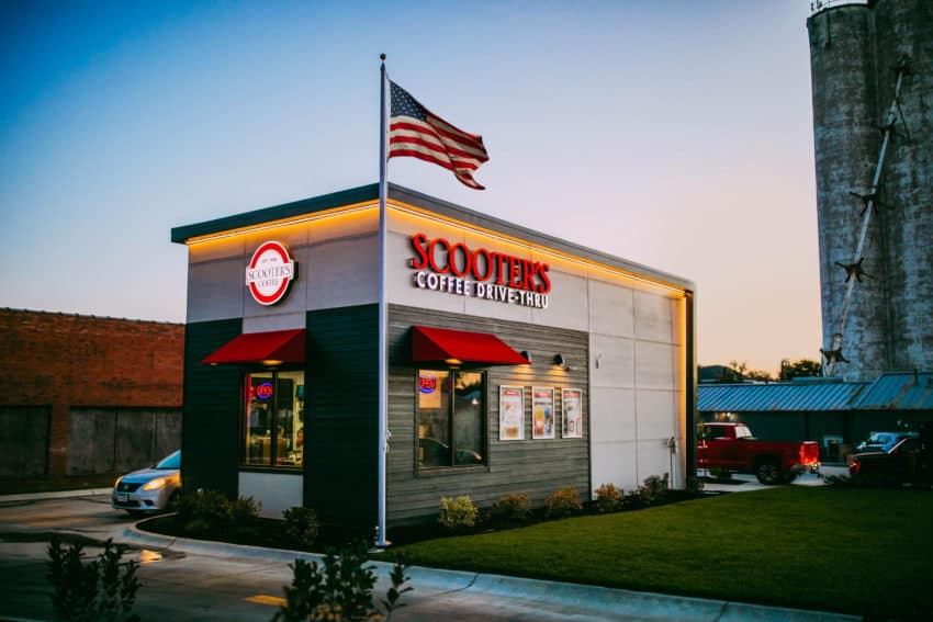 A scooters coffee kiosk seen at sunset with an American flag flying out front.